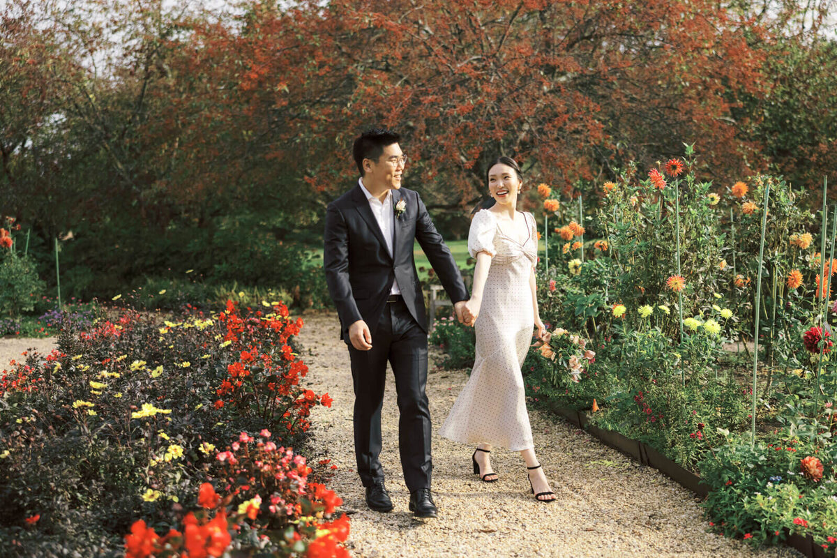 The engaged couple is walking happily amidst the foliage and colorful flowers in orange and yellow hues. Image by Jenny Fu Studio