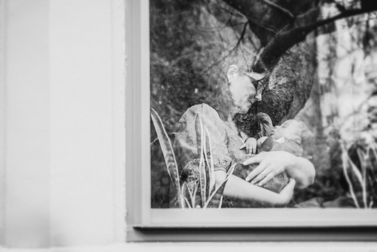 A parent holding a small child seen through a window