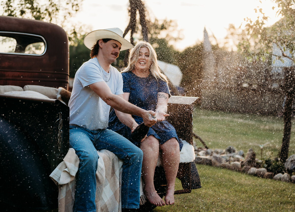 champagne spraying from the bottle while engaged couple celebrate