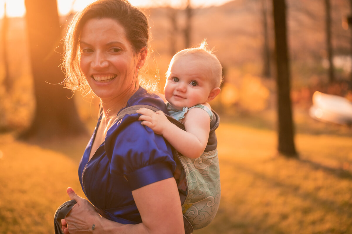 Mom with baby  in carrier at golden hour sunset smiling