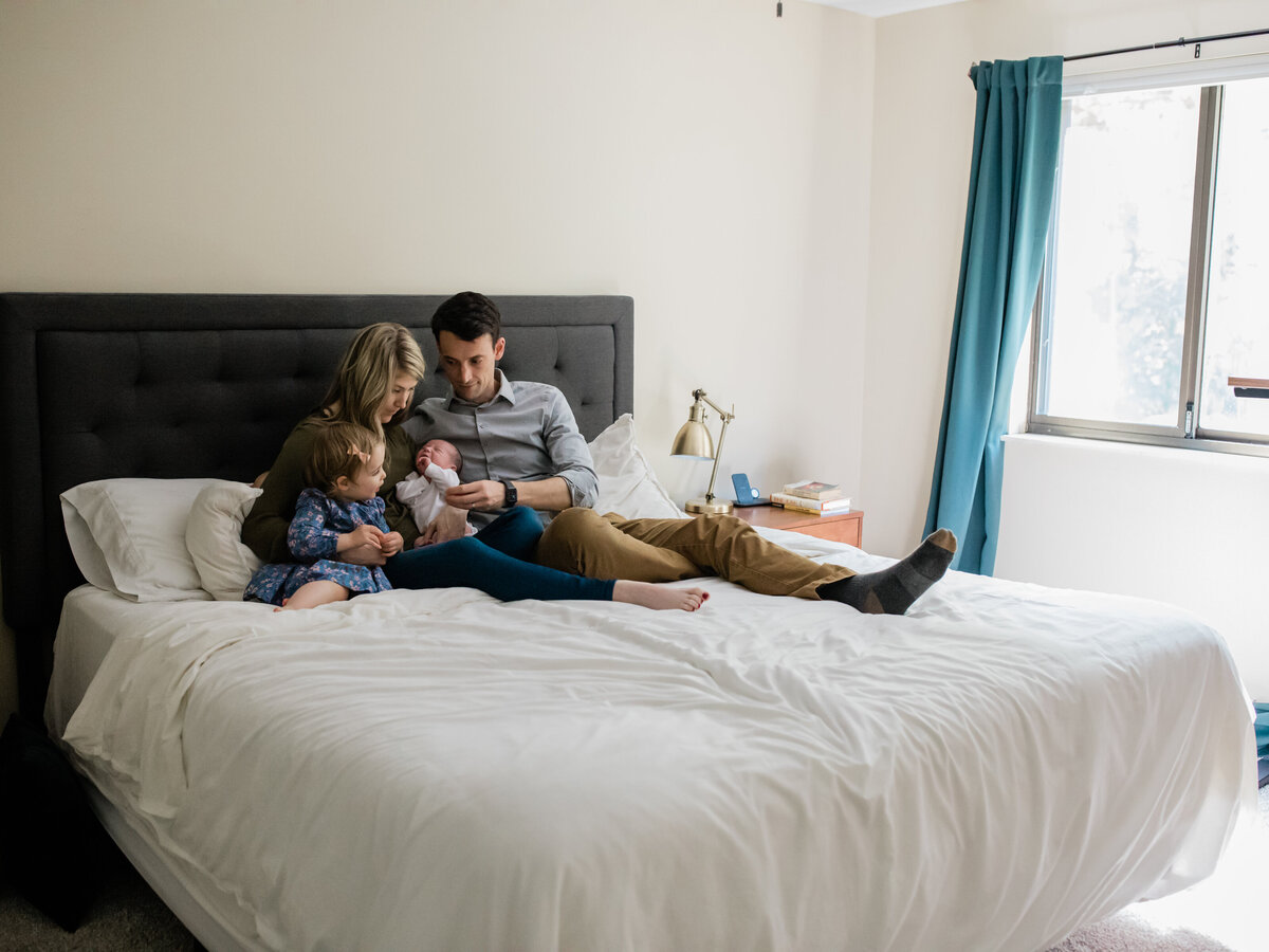 family sitting on bed for newborn in home lifestyle photography session cleveland newborn photographer