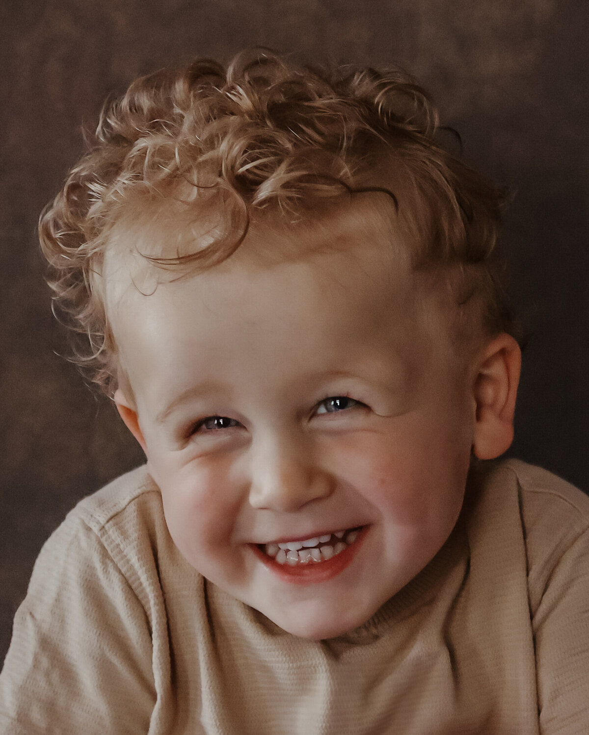 schattig vrolijk jongetje, portret gefotografeerd tegen een lichtbruine achtergrond