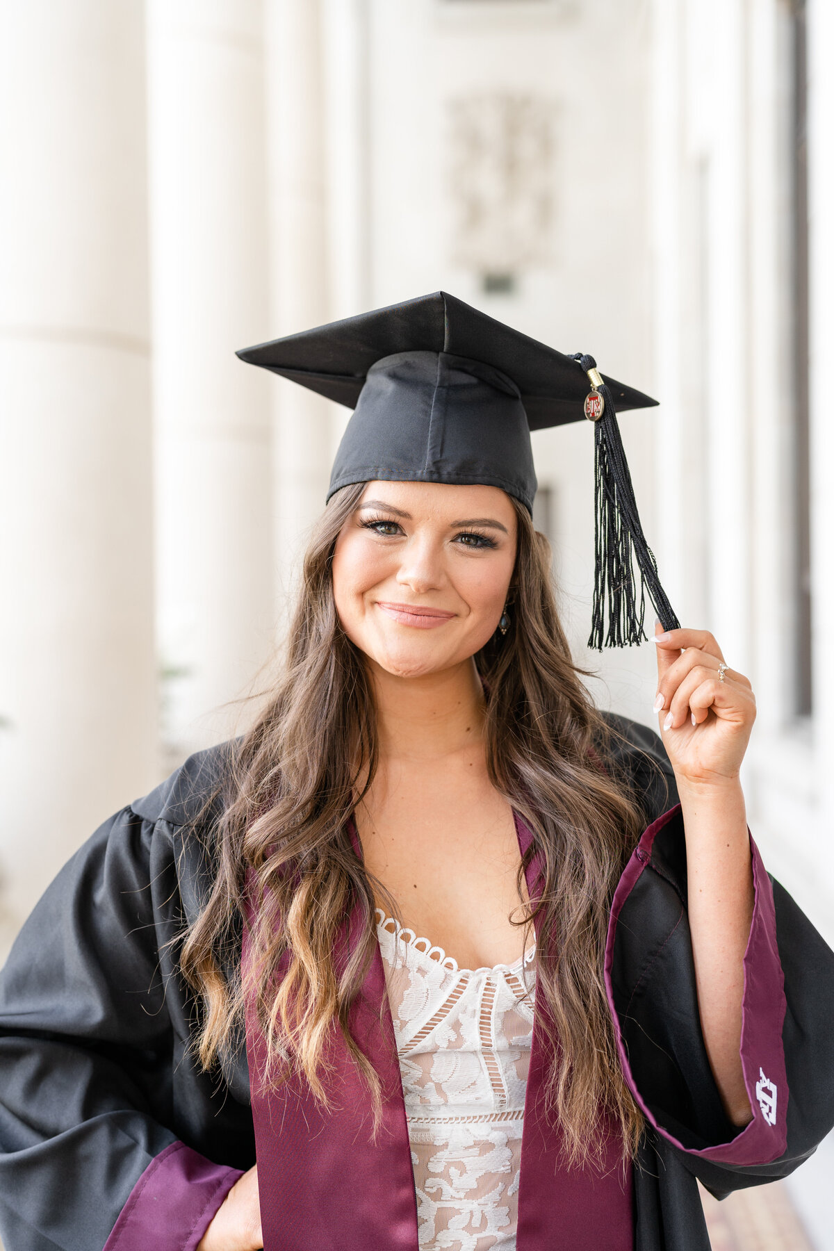 Texas A&M senior girl smiling and wearing cap, gown and stole in the Administration Building columns