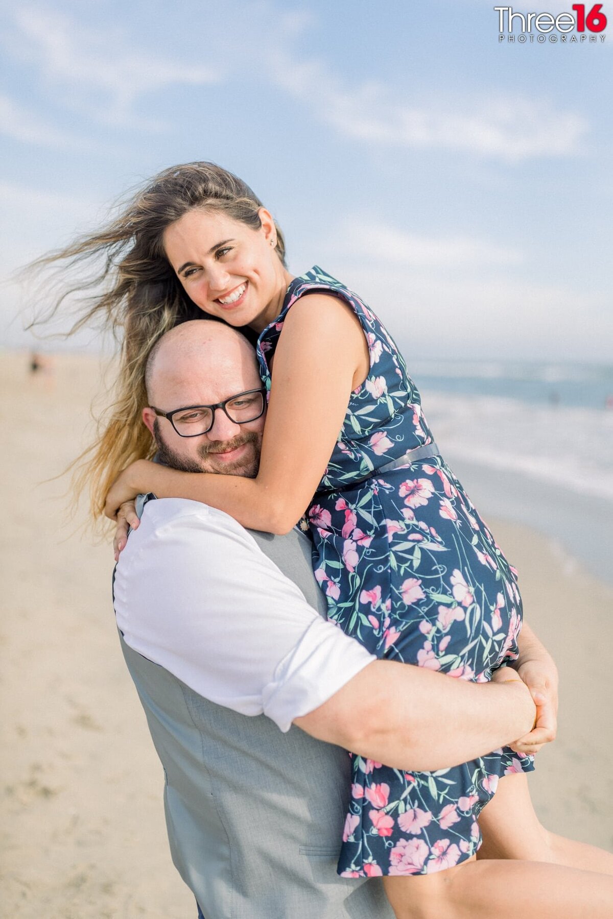 Groom to be lifts up his Bride in his arms while standing on the beach.