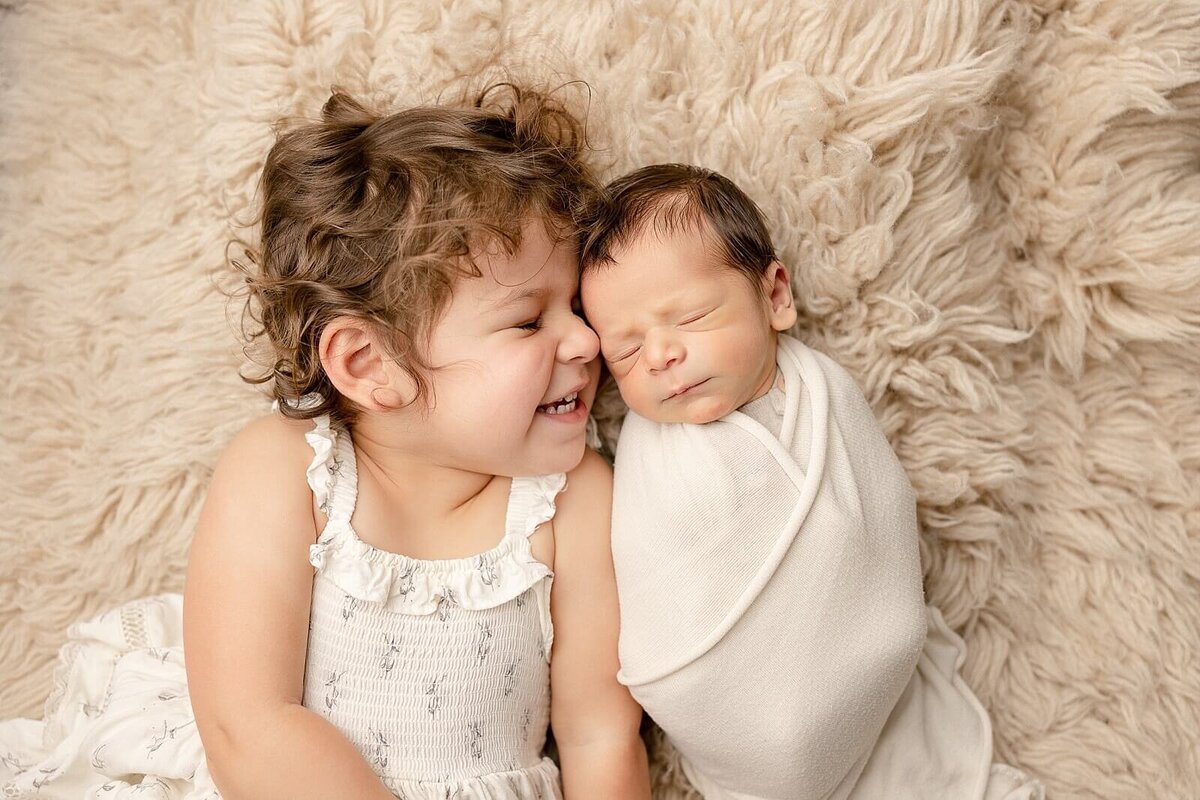 big sister smiling at baby brother sleeping on rug