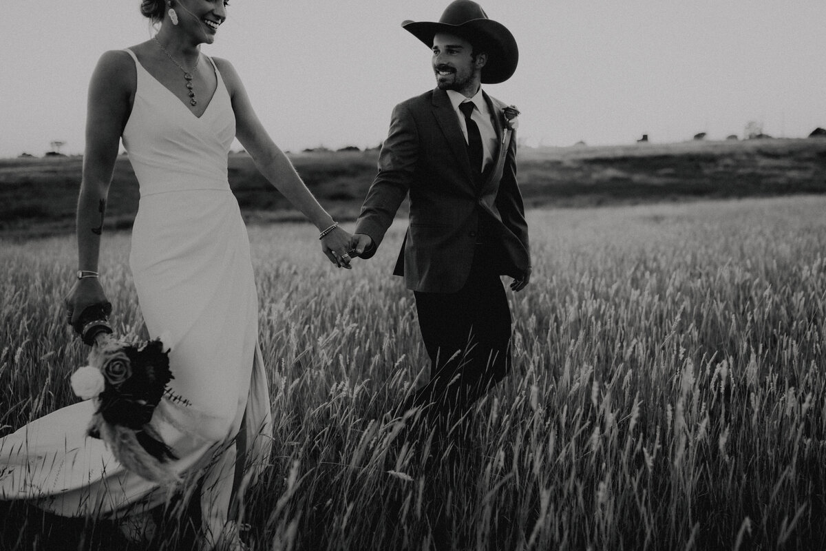couple walking hand in hand through a field taken by oklahoma wedding photographer