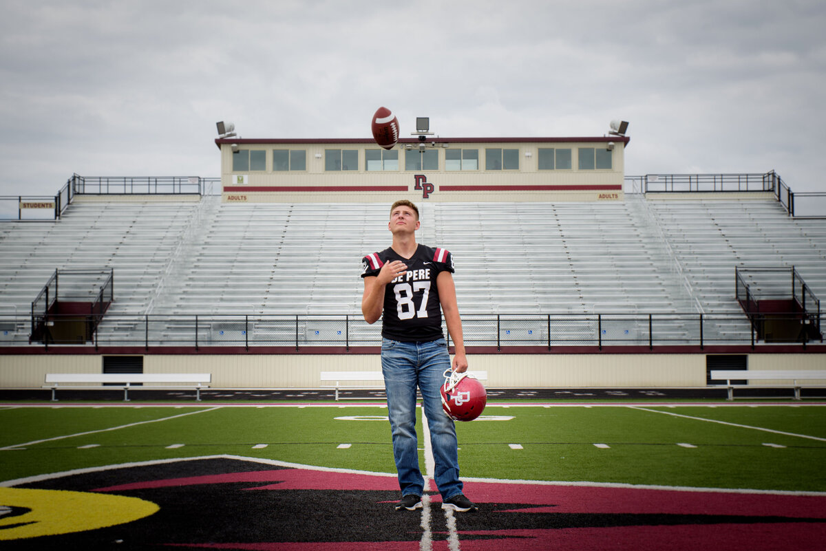 De Pere High School senior boy wearing his football jersey standing at the De Pere Redbird High School Football Stadium