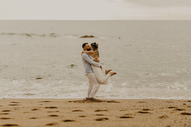 Femme sautant dans les bras de son chéri dans un décor de plage. Capturés par Laura, photographe couple en Vendée.