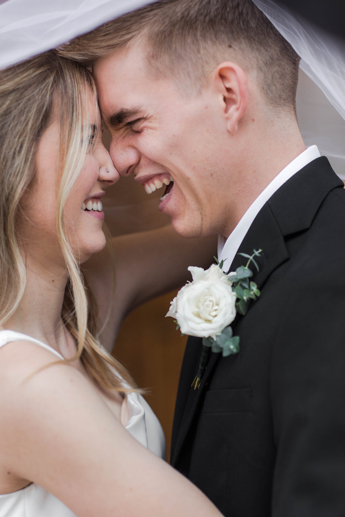 bride and groom laughing under veil