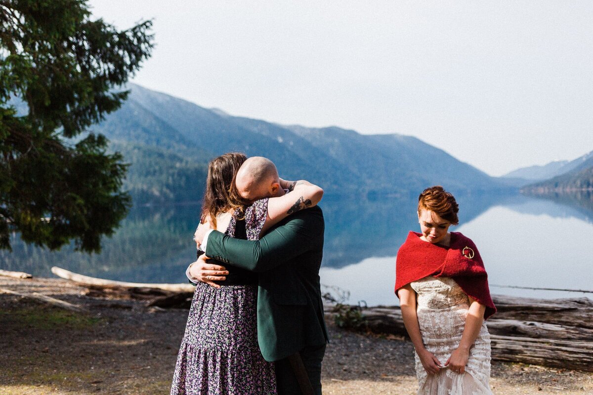 A groom hugging his sister after elopement at Lake Crescent with bride standing aside.
