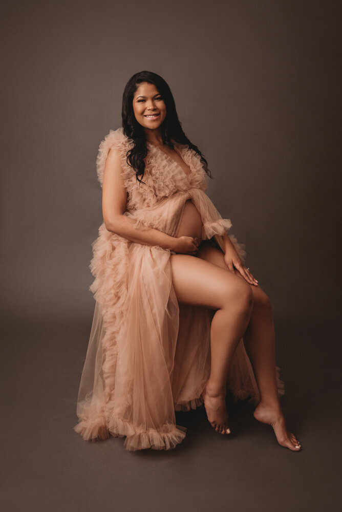 Maternity session with Atlanta, Georgia maternity photographer pregnant woman holding baby bump wearing pink ruffle sheer maternity  dress on dark grey color backdrop