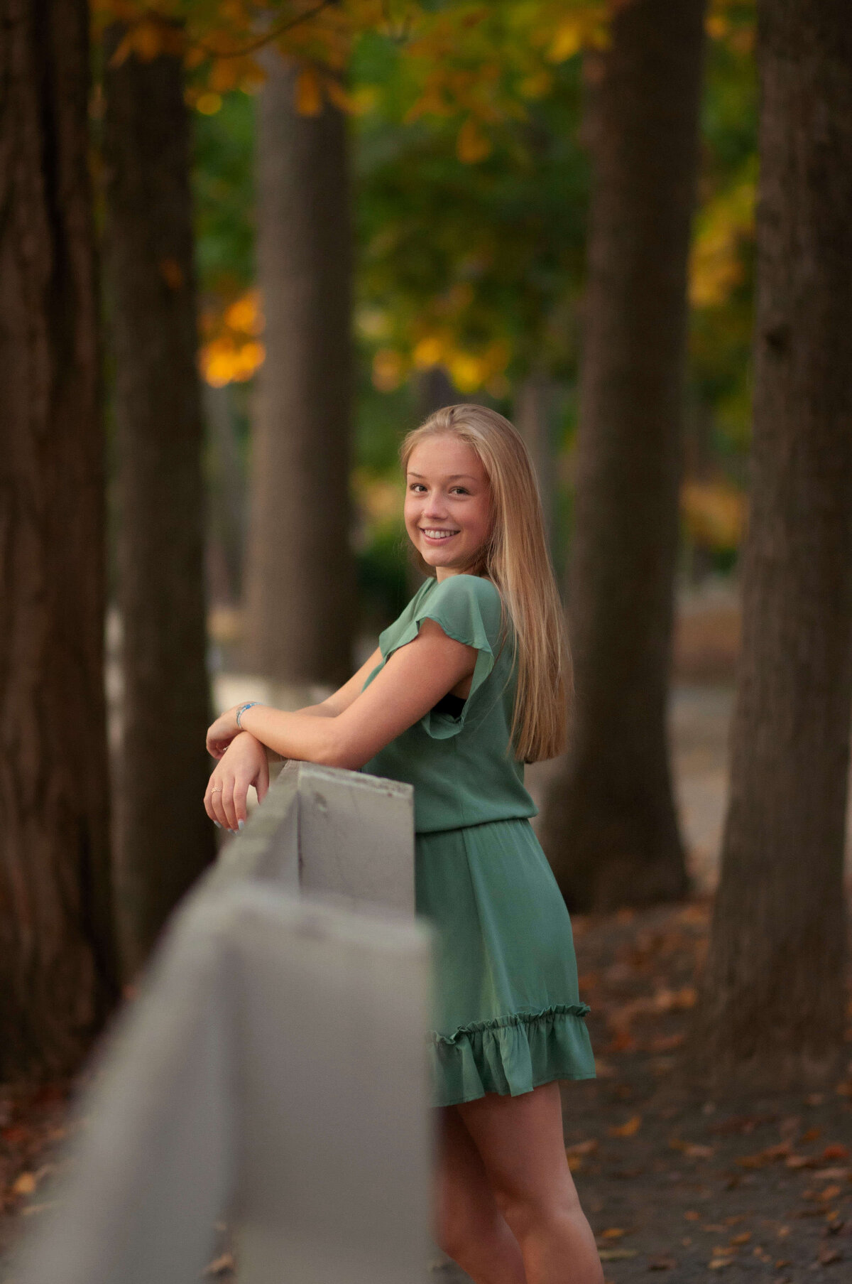 A girl with a green dress smiles at the camera with fall colors around her at Endicott Park.