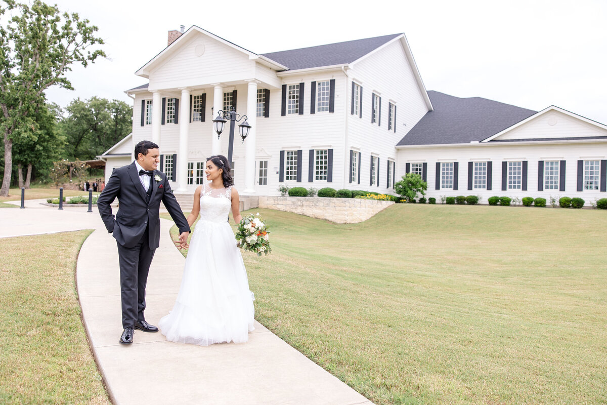 bride and groom walk from Aubrey Mansion at Texas wedding by Firefly Photography