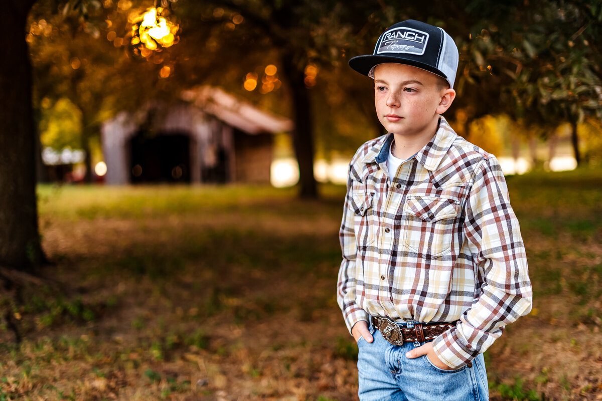 County boy in a plaid shirt in front of a barn at sunset in Gilmer, Texas