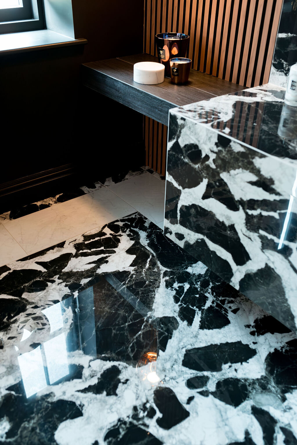 A close-up view of the marble countertop in a dark, modern bathroom. The marble extends to the flooring. To the left, there is a wooden slatted wall.