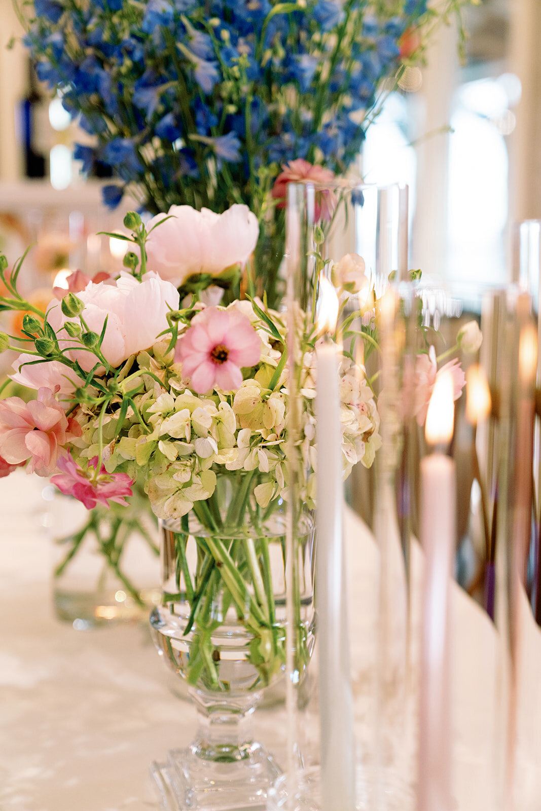 Close-up of a colorful floral centerpiece with pink anemones, green hydrangeas, and tall taper candles in glass holders at Burritt on the Mountain wedding reception.