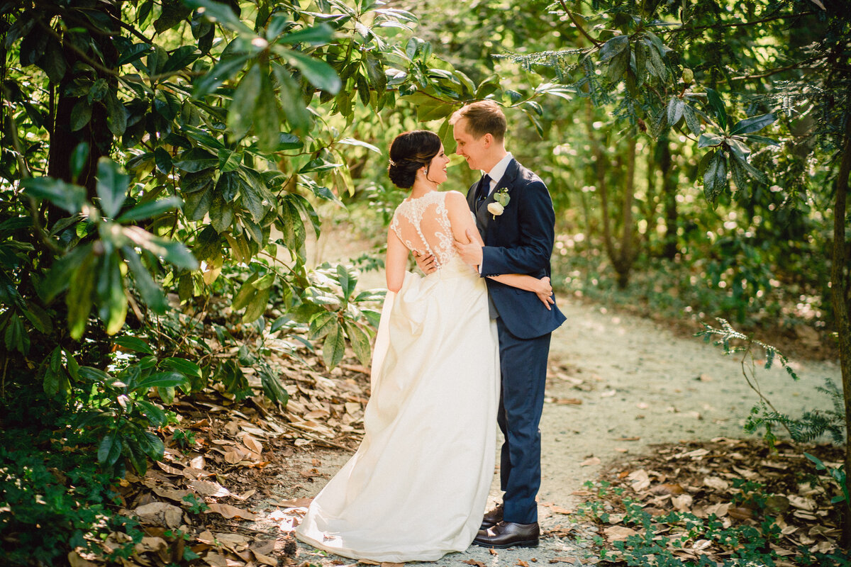 A wedding couple hugging and about to kiss on a path in the woods.