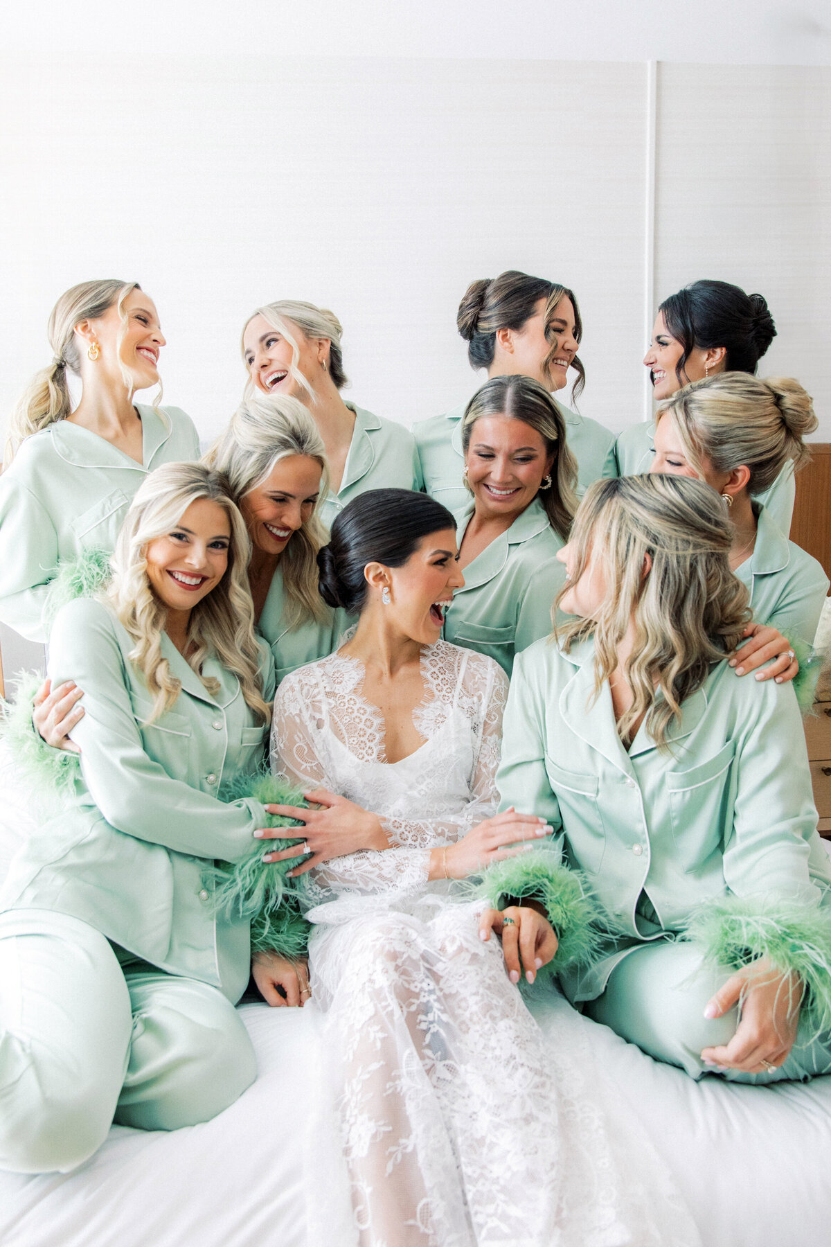 Brides surrounded by bridesmaids on bed laughing