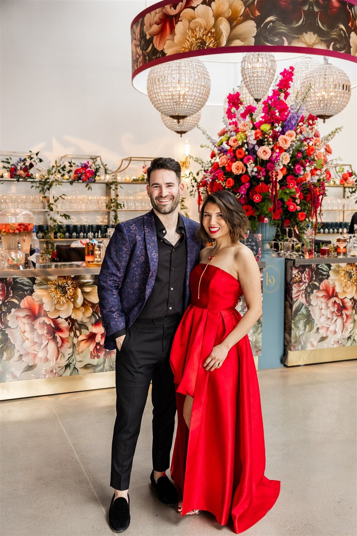 Large gathering at a Baroque-themed event, with guests dressed in formal attire mingling amid lavish decor including gilded furniture, crystal chandeliers, and rich drapery in a grand, ornately detailed space