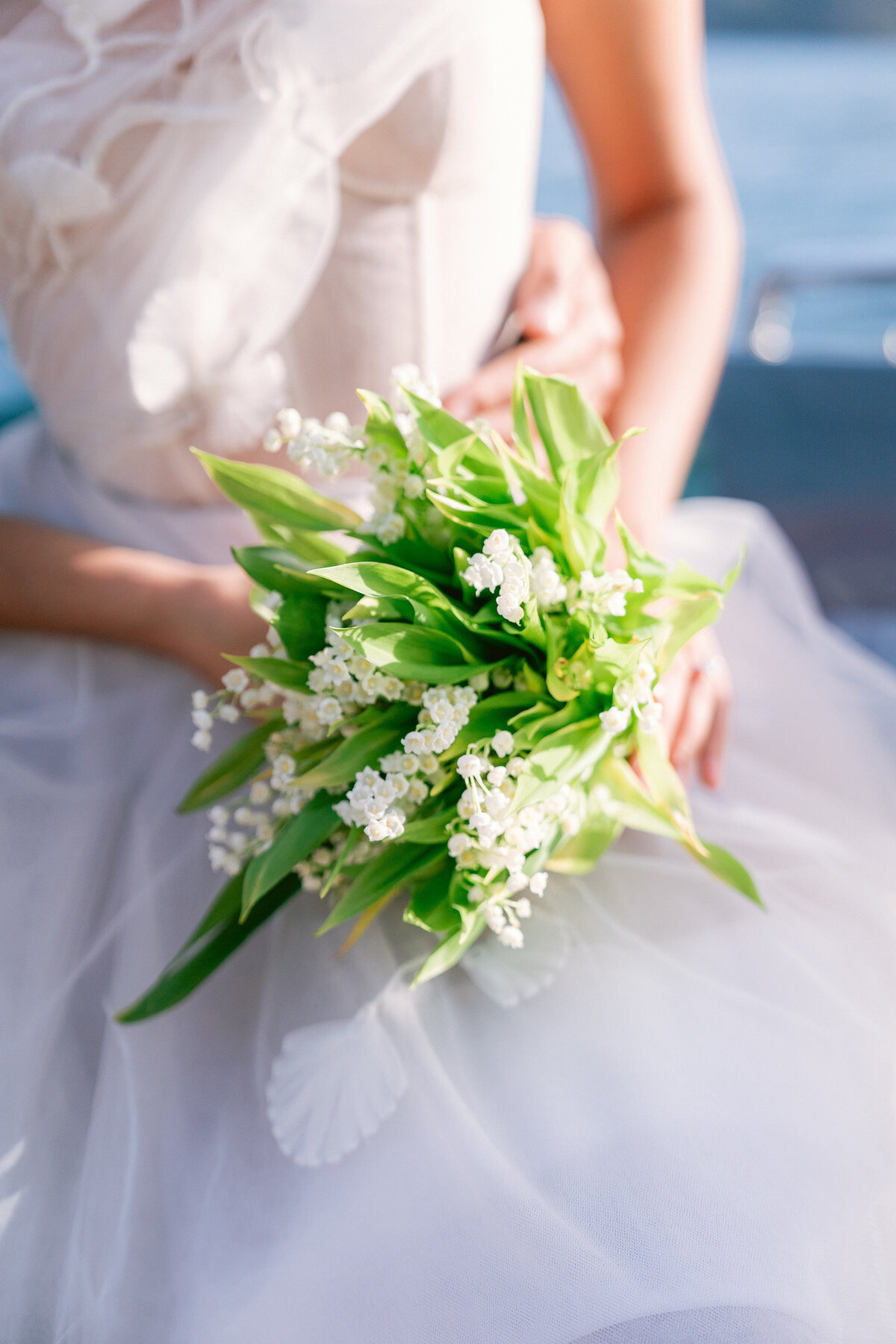 Bride holding small bouquet of white florals with greenery on a private boat on lake como, italy