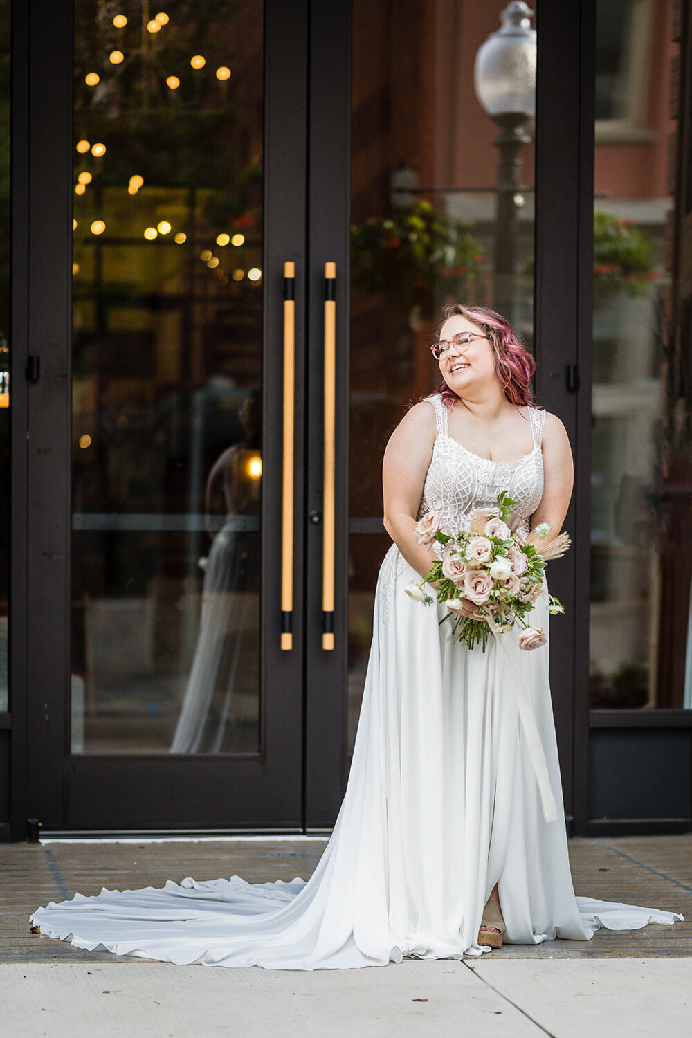 A bride in a long wedding dress holds her bouquet in front of her and looks towards her right past her shoulder and smiles widely on her elopement day in Downtown Roanoke.