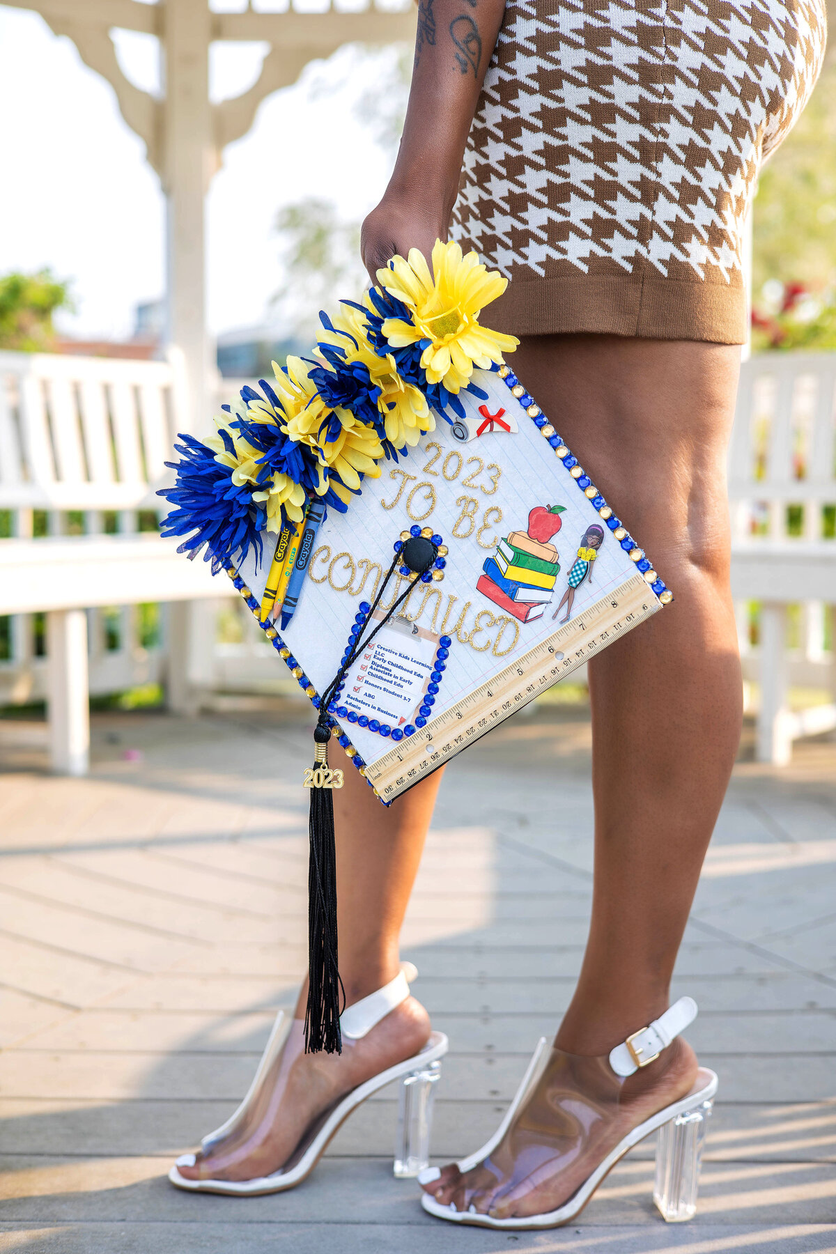 College graduate standing holding decorated graduation cap in front of her legs