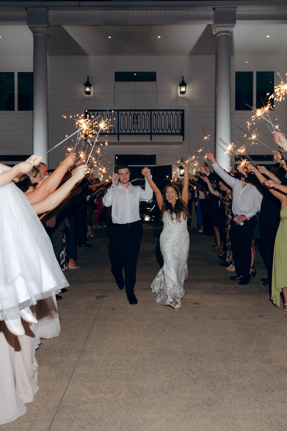 A wedding photo of the bride and groom leaving the wedding reception while guests hold sparklers in the air celebrating