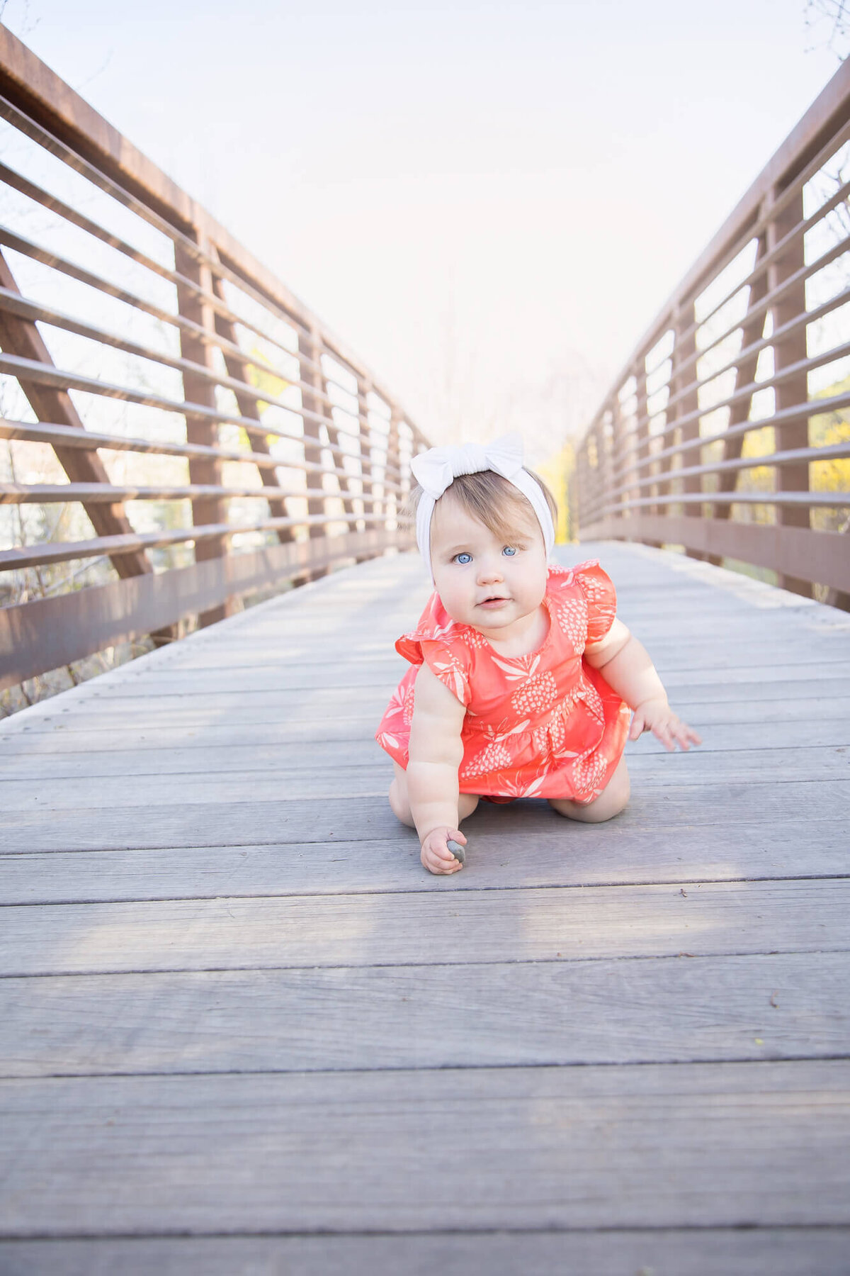 baby girl in orange dress crawling on a bridge