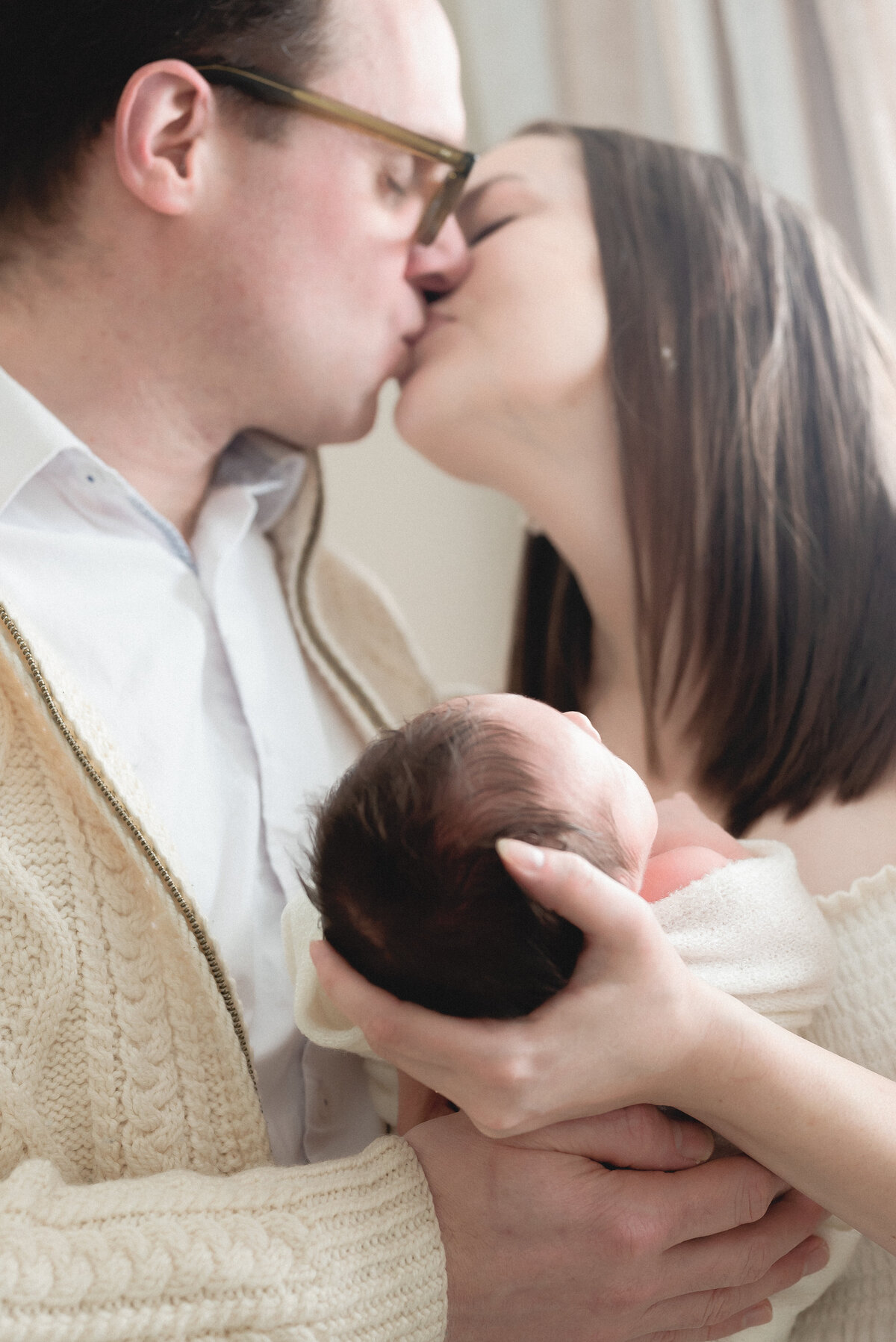 Mother and father kissing while holding newborn baby
