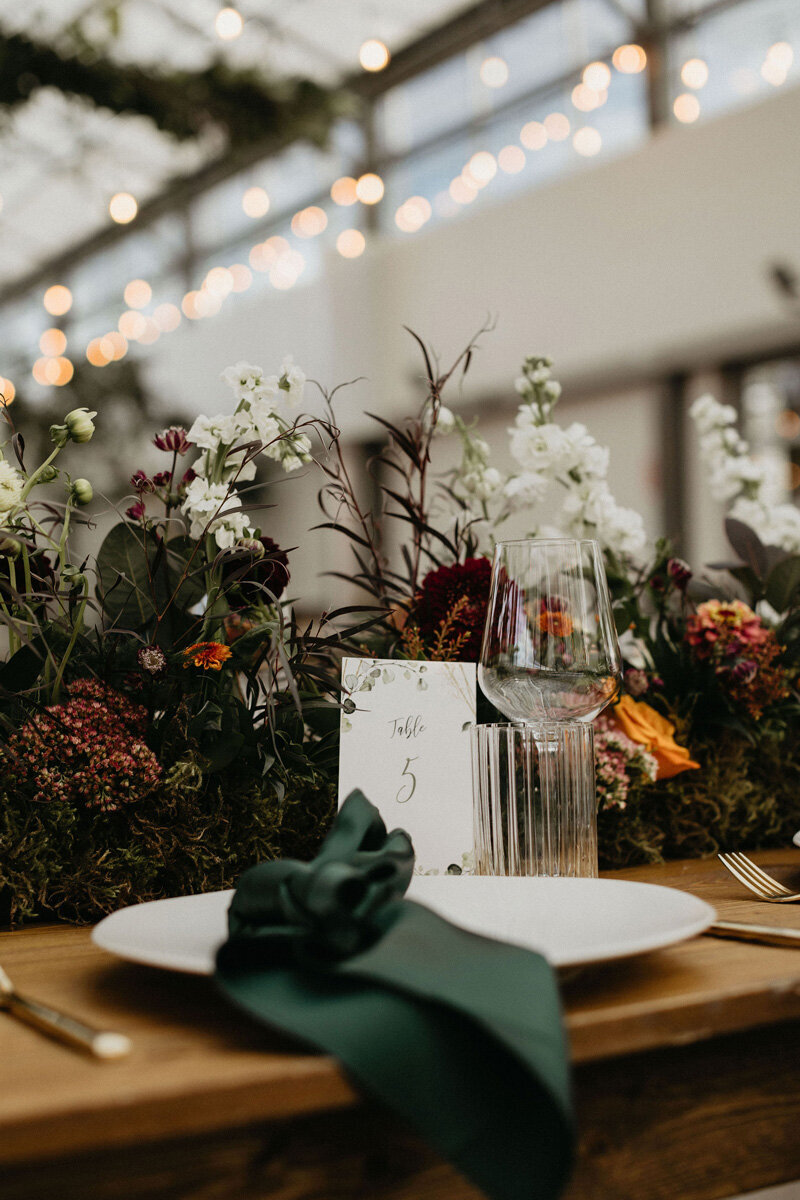 Close up of wedding reception table setting with rich jewel tones and greenery.