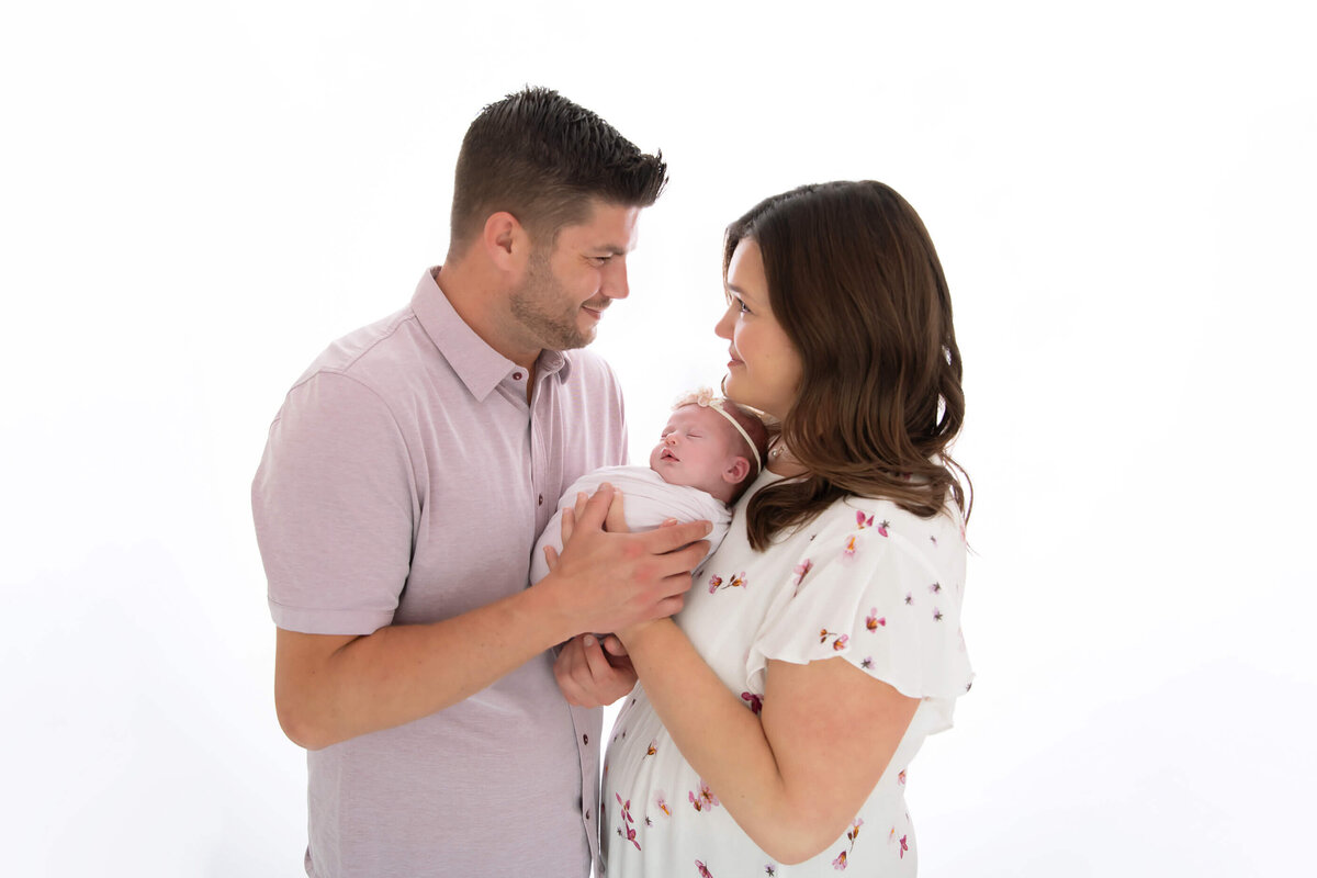 husband and wife holding newborn baby girl against a white background for their family newborn photography session.