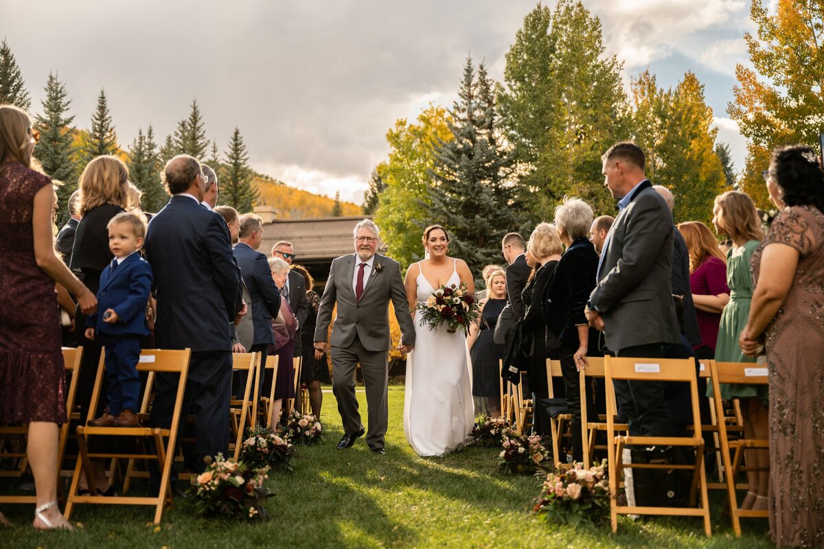 Bride walks down the aisle with her father on their wedding day in Vail, Colorado.