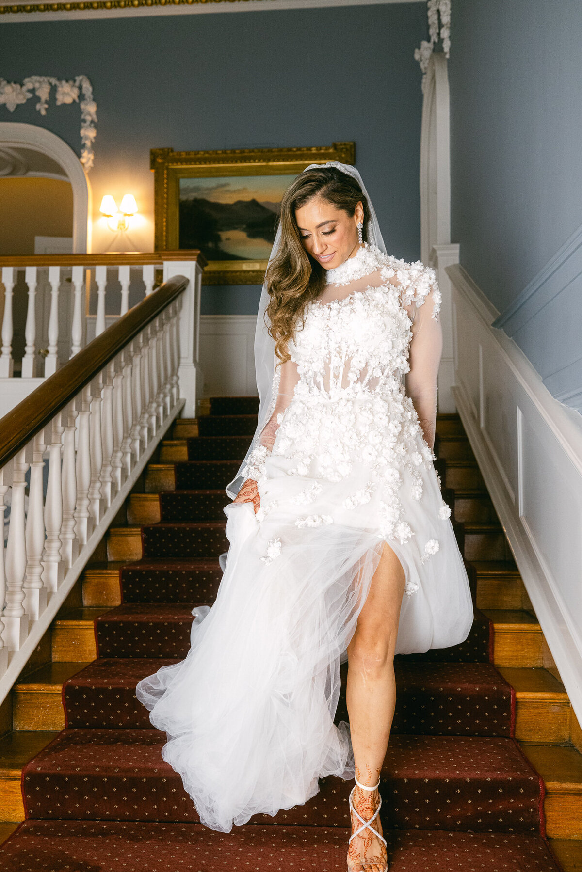A wedding photo of the bride walking down a staircase in her white wedding dress
