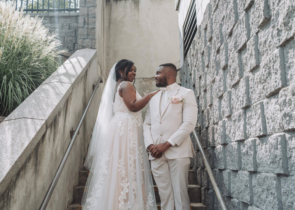 Bride and groom sharing a joyful moment on the steps at Massanutten Resort Conference Center in Massanutten, Virginia. The bride is wearing a lace wedding dress and veil, while the groom is dressed in a light-colored suit with a pink boutonniere. Shot by Quinn Photography LLC.