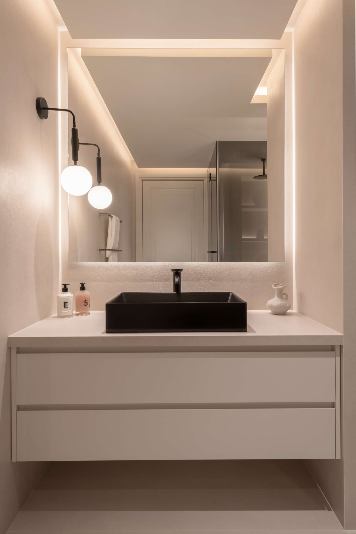 A modern bathroom with a focus on light, neutral tones. A stark black sink adds contrast and intrigue to the space.