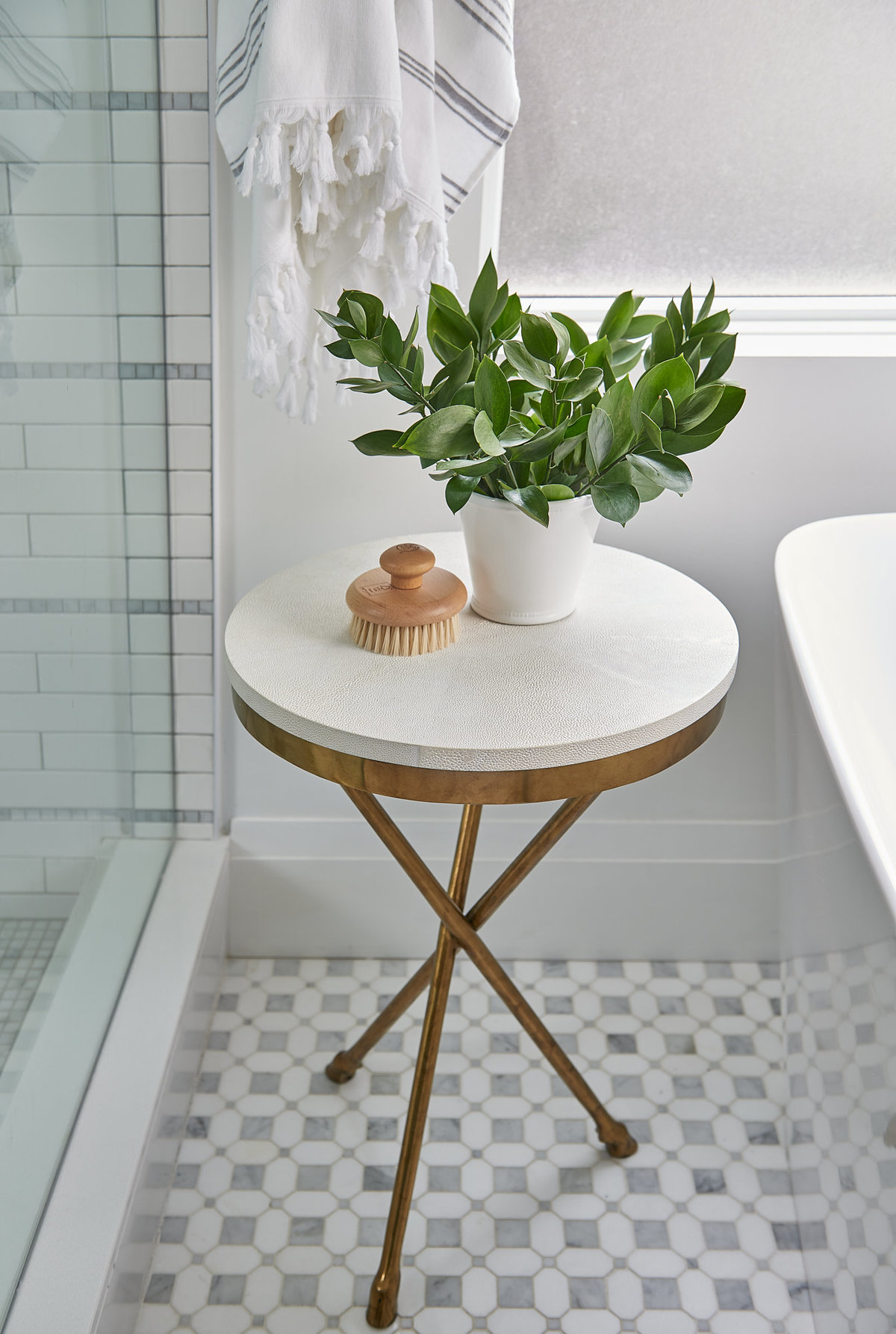 Bathroom with marble mosaic floor and gold side table styled with plant