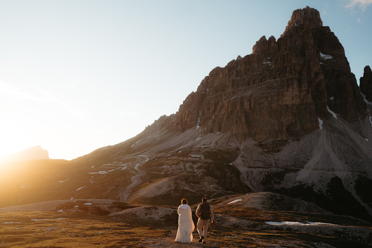 Dolomites wedding couple walks towards a mountain with the sunset glowing golden around them