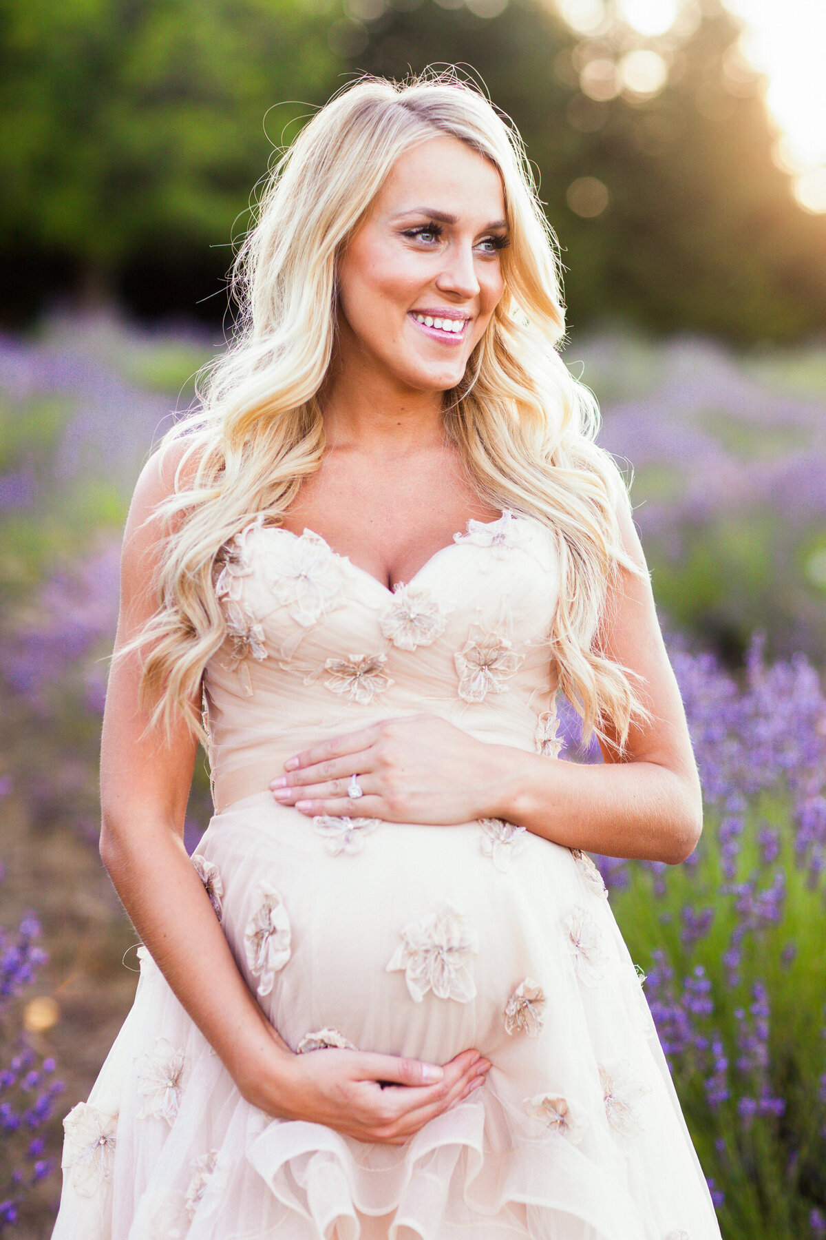 pregnant woman holding baby bump for maternity photography session in lavender field