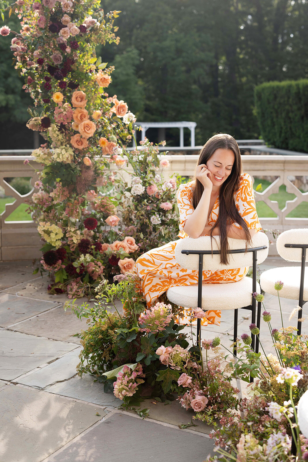 Amanda seated among garden florals in orange, blush, and burgundy at a wedding she designed