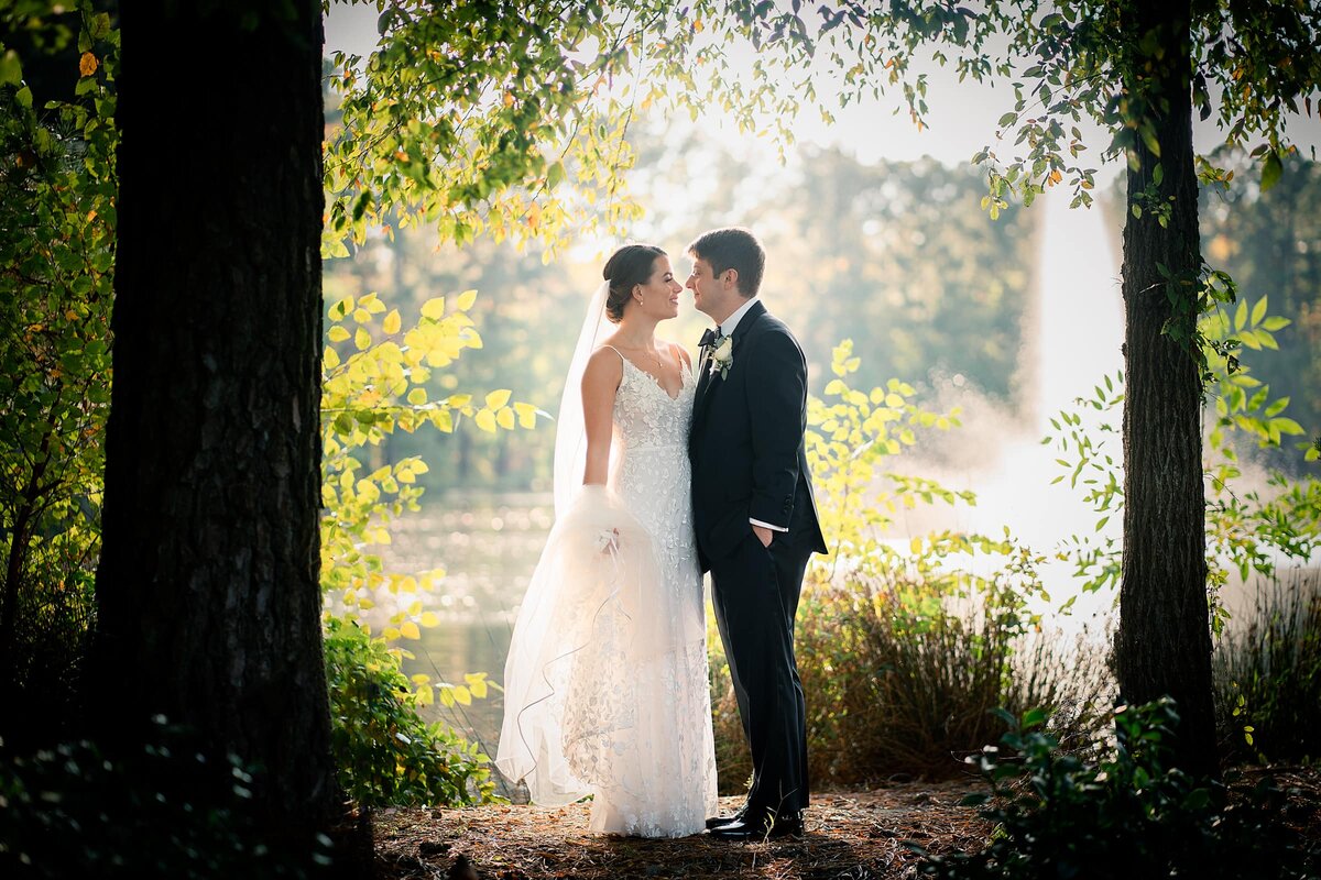 A wedding couple standing in front of a lake about to kiss.