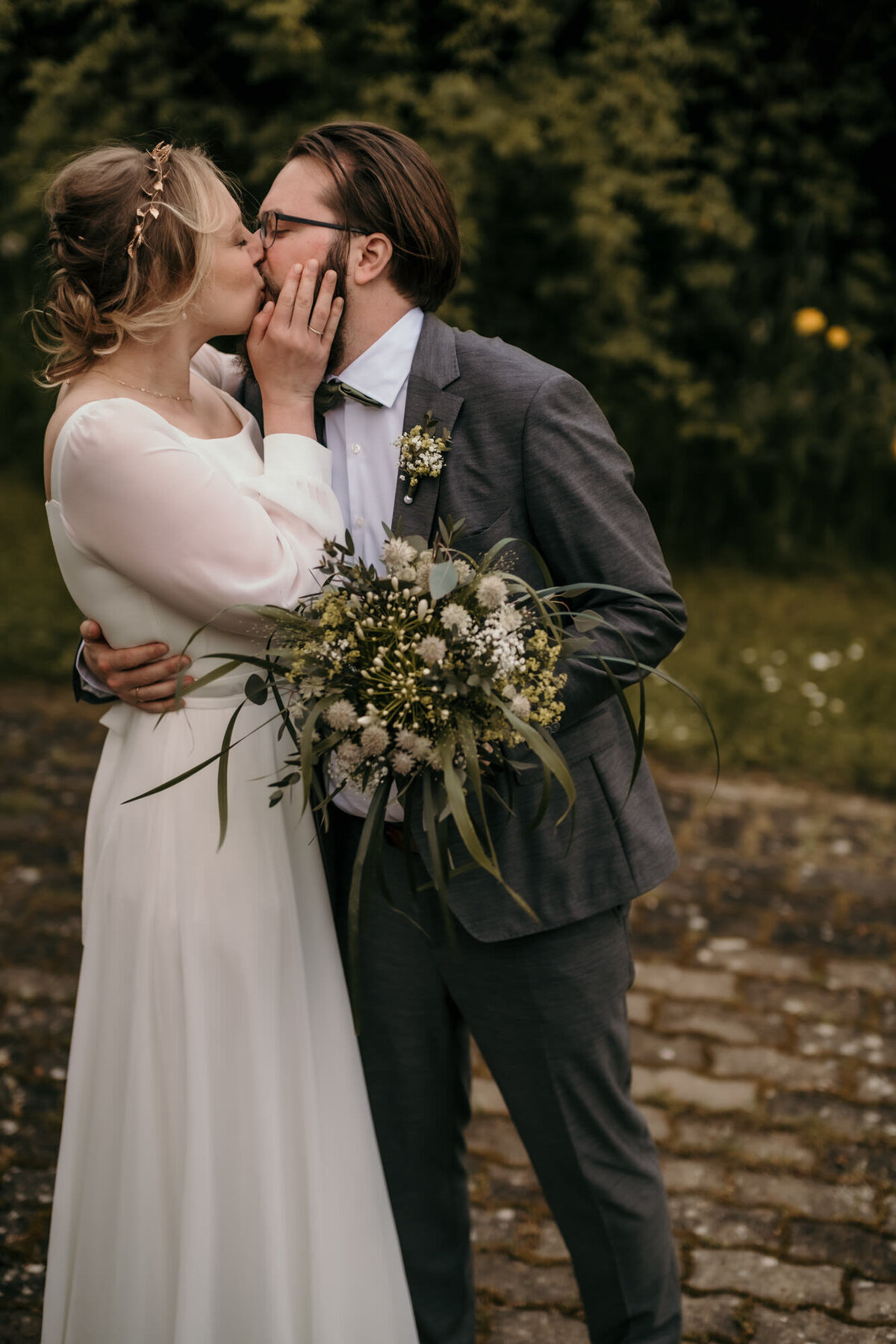 Der Bräutigam lehnt sich, den Brautstrauß haltend, leicht zu seiner Braut, während sie sich Küssen.