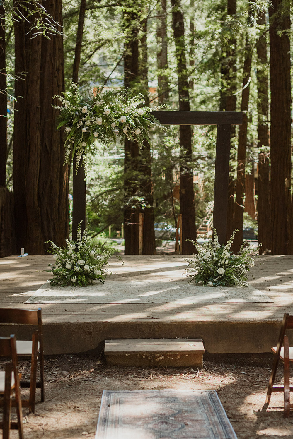 Woodland wedding altar with greenery and floral arrangements on wooden stage