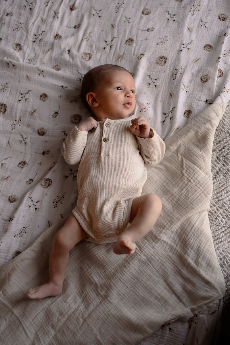 Pasgeboren baby ligt op bed en kijkt op zij tijdens een newbornshoot in Apeldoorn
