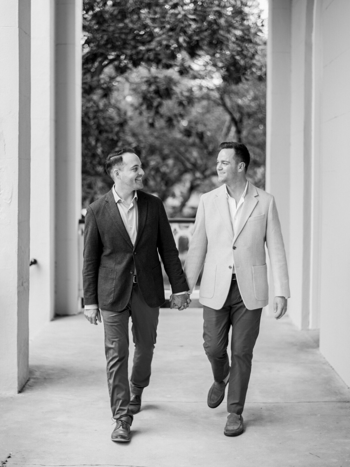 A charming black-and-white image capturing a couple holding hands, strolling down a serene pathway in Charleston lined with soft natural light, embodying love and companionship.
