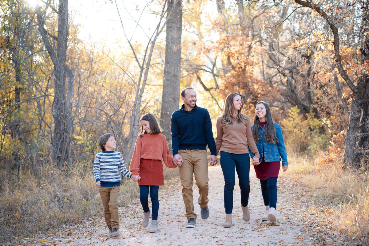 A family of 5 holds hands while exploring a park trail at sunset in fall