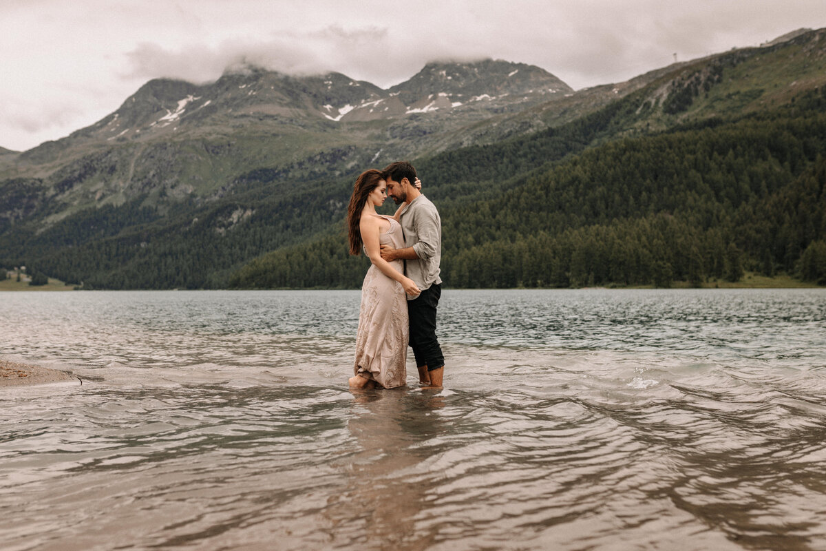 Liebespaar in inniger Pose steht in einem See in der Schweiz mit Bergen dahinter
