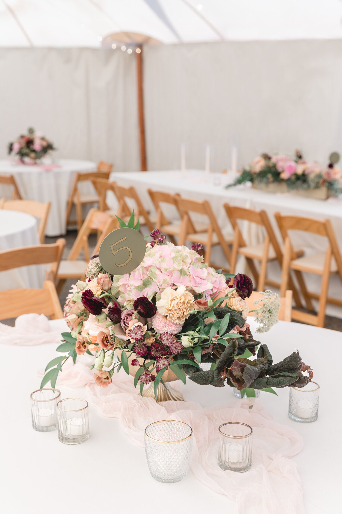 Peach, blush, and green centerpiece surrounded by candles under a sail cloth tent