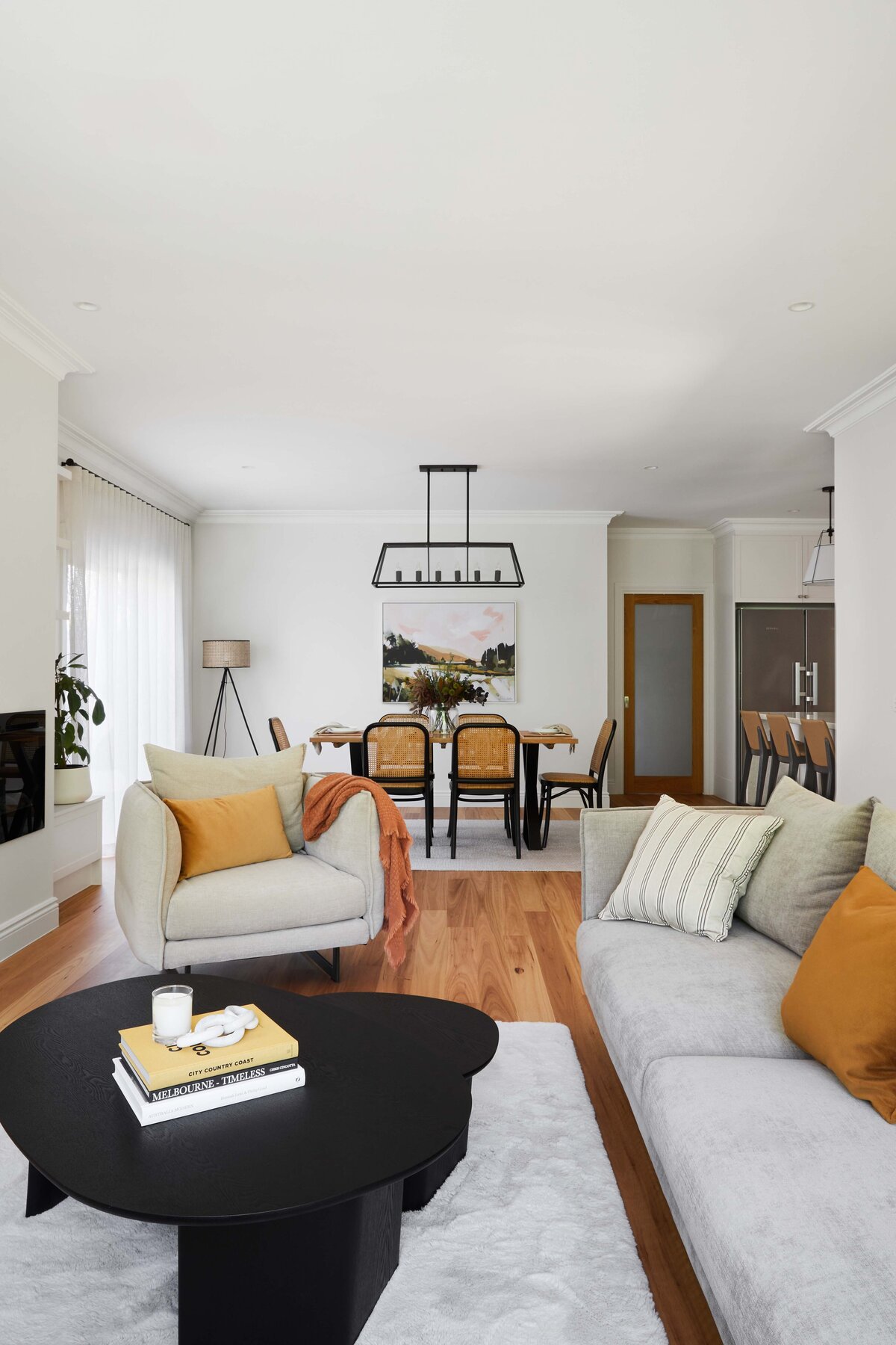 View from living to dining with white walls, soft grey seating, black coffee table, cane chairs and black pendant lighting styled in a Williamstown interior.