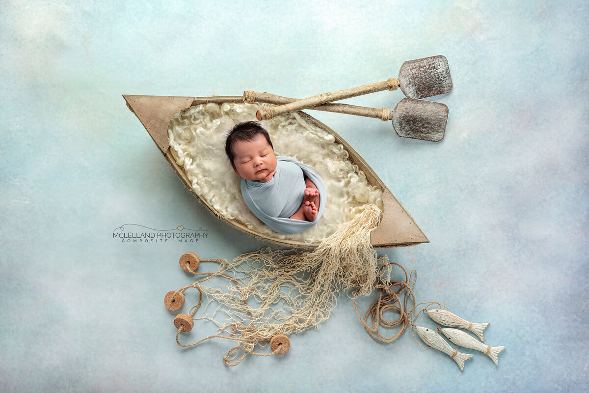 Newborn boy wrapped in blue inside a rustic wooden boat 