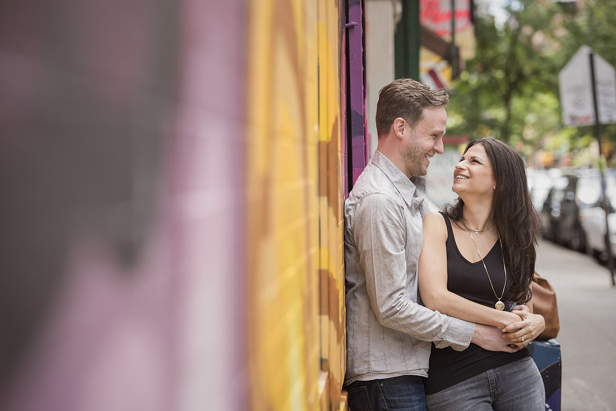A couple with their arms around each other as they lean on a mural